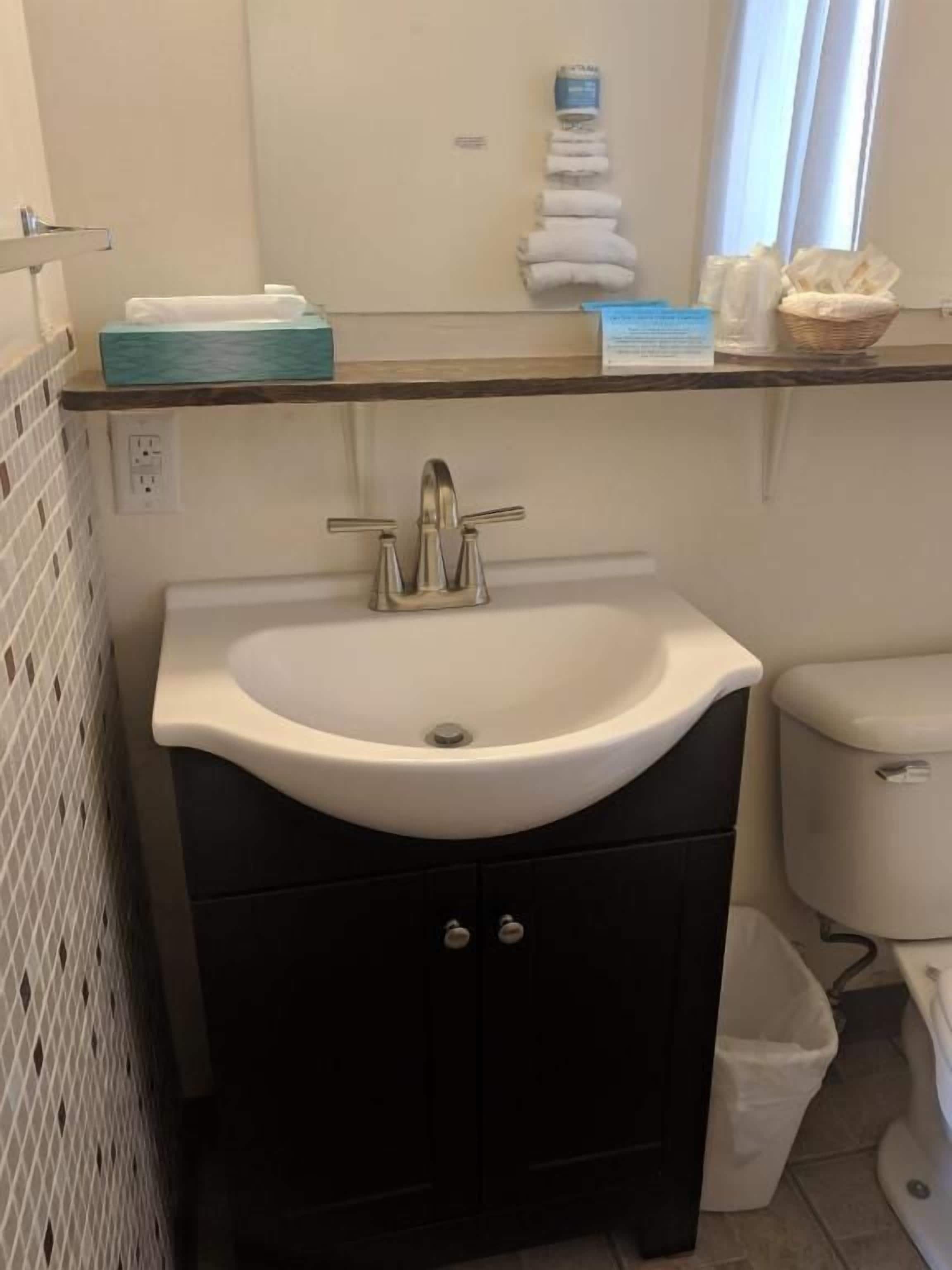 A bathroom with a white sink, black cabinets, a white toilet, and a window with curtains.