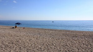 A beach with a person under an umbrella, a boat in the distance, and a clear sky. - Casa Pozzillo: two rooms with splendid sea right in front of the house! (Acireale)