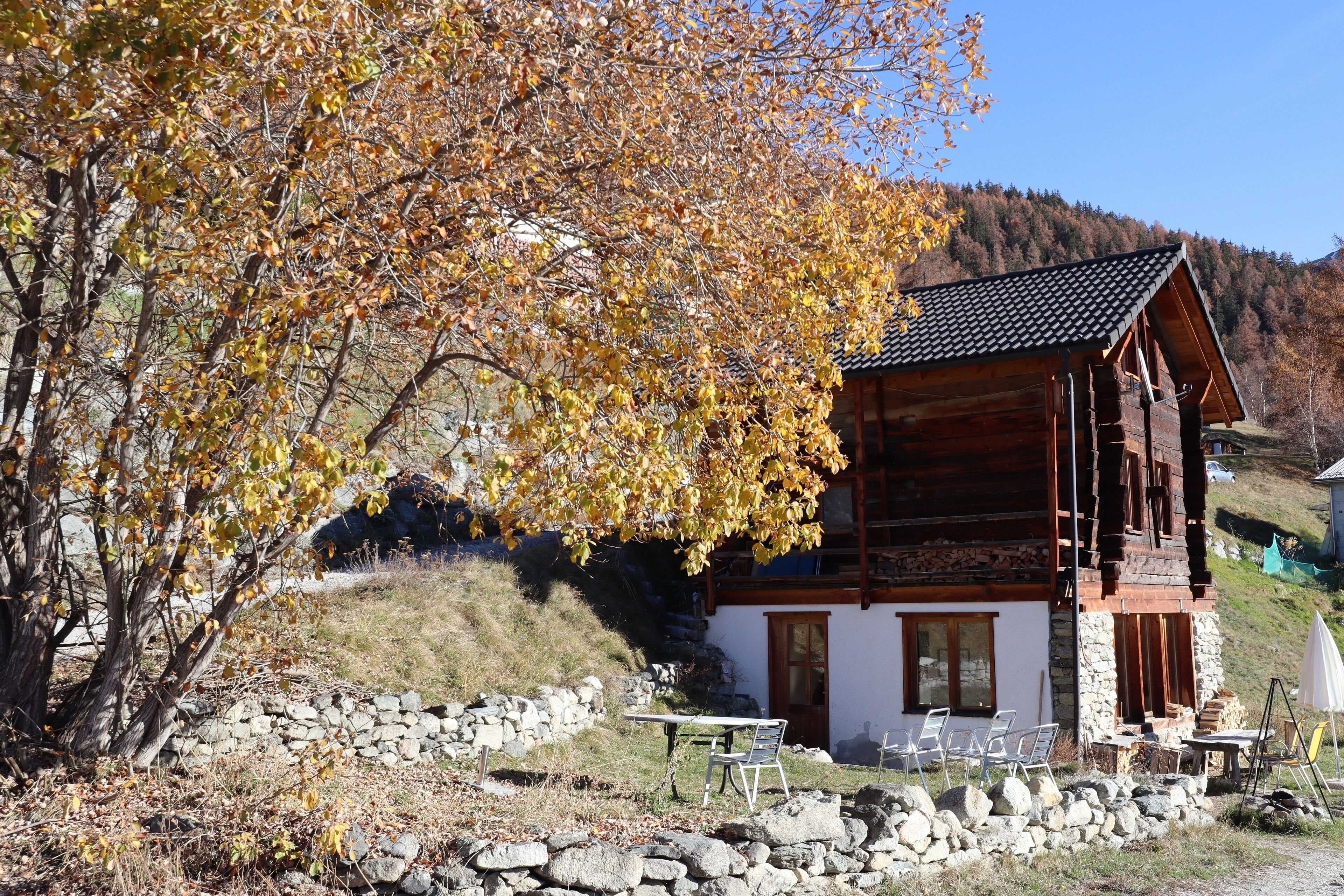 Una baita di legno con fondamenta in pietra, una zona pranzo con posti a sedere all'aperto e vista su una collina.