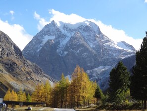 Un paysage de montagne avec des sommets enneigés, des arbres aux couleurs automnales et un ciel dégagé.