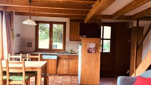 Une cuisine chaleureuse avec des meubles en bois, une table à manger avec des chaises, un four encastré et un téléviseur fixé au mur.