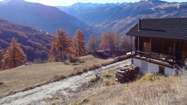Une cabane rustique, dotée d’un toit en pente, entourée d’un paysage montagneux et de quelques arbres clairsemés.