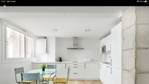 A modern kitchen with white cabinets, a wooden floor, and a dining area with a glass table and metal chairs. - CRUISE APARTAMENT. First line beach. It will look like it's on a boat. (Málaga)