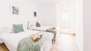 A bright, minimalist bedroom with two beds, a large window, and a hanging light fixture. - CRUISE APARTAMENT. First line beach. It will look like it's on a boat. (Málaga)