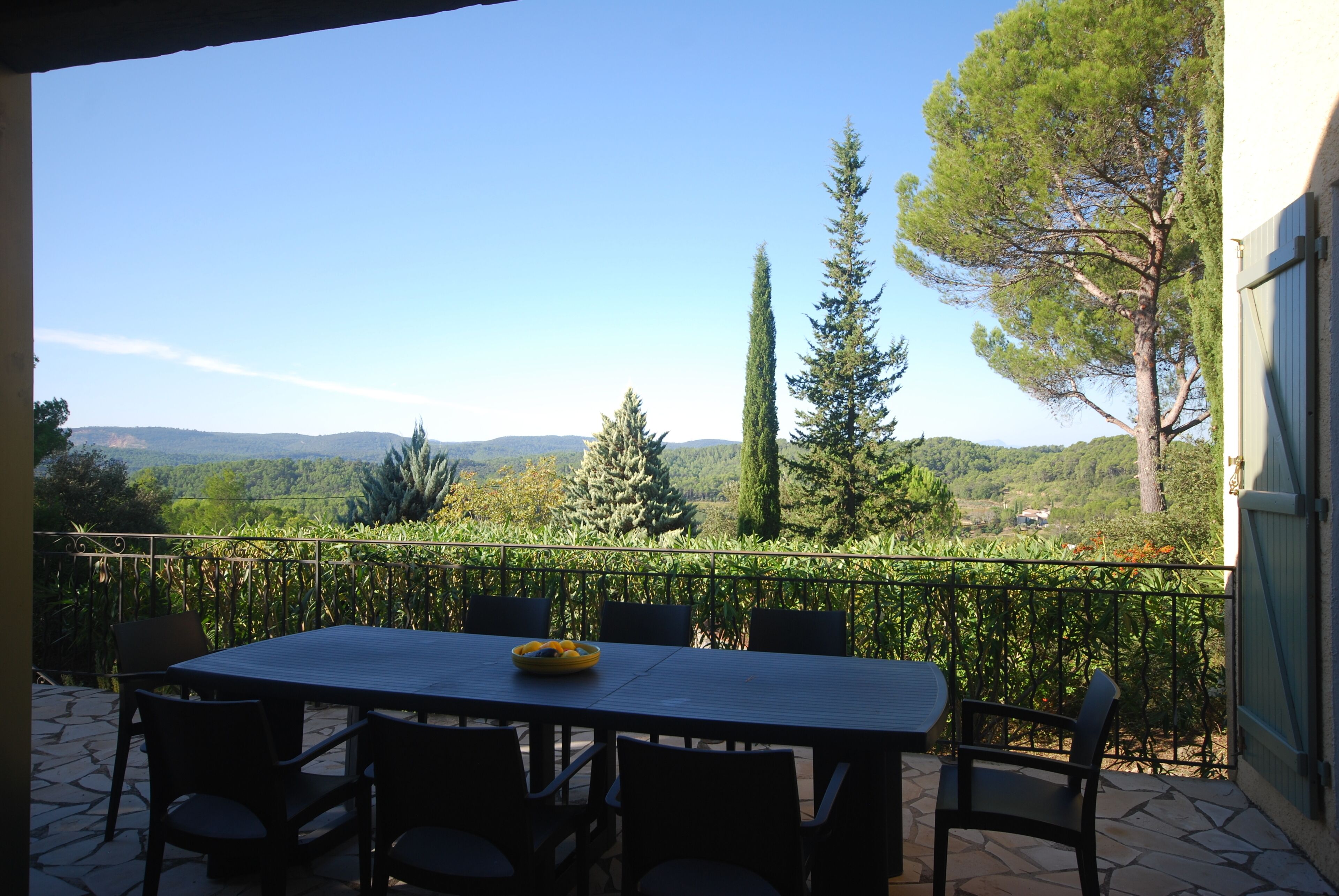 Une terrasse extérieure avec une table et des chaises, offrant une vue sur un paysage pittoresque composé d’arbres et de collines.