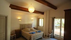 Ein Schlafzimmer mit Bett, Nachttischen, einer Pendelleuchte, einem Fenster mit Vorhängen und einer Tür zu einem Außenbereich.