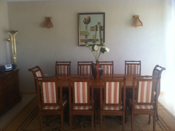 A dining area with a wooden table and six chairs, a vase with flowers, and two wall-mounted lamps. - Impressive family villa with private pool, barbeque, sun terrace, sauna and gym (Branishte)