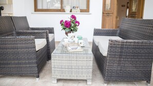 A wicker sofa set with a matching ottoman, a small table with a vase of flowers, and a window with curtains in the background. - Villa Marina for rent in Kathikas,Paphos ..Family friendly near Coral Bay. (Paphos)