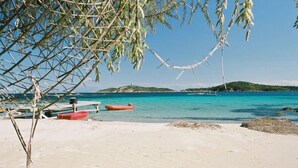 Una playa con agua turquesa cristalina, una orilla arenosa y un barco pequeño a lo lejos.