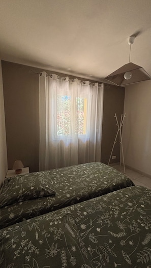 A bedroom with two beds, a window with sheer curtains, and a ceiling fan.
