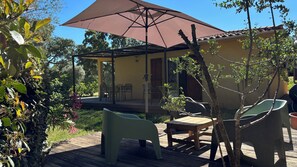 Une terrasse extérieure dotée d’un espace salon couvert, de meubles en bois et d’une pergola surmontée d’une toile de couleur marron.