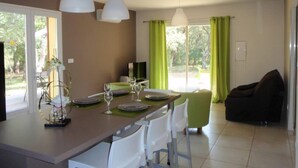 Un comedor con una mesa preparada para cuatro, sillas blancas, un televisor y un sofá al fondo.