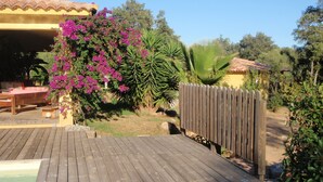 Una terraza de madera que conduce a una zona de piscina con un espacio de estar techado y una valla de madera.