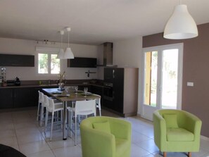 A modern kitchen with a dining area, featuring a large island, white chairs, and green armchairs.