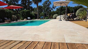 Una piscina con muelle de madera, sillas de descanso y sombrillas.