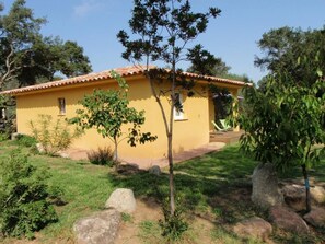 A yellow building with a tiled roof, surrounded by greenery and rocks.