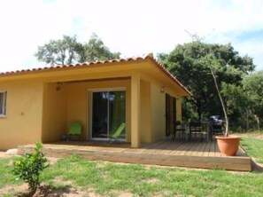 A yellow building with a tiled roof, a covered patio, and a small garden area.