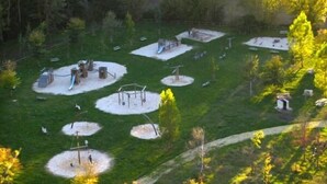 Un parc doté de diverses installations de jeux et d’espaces verts ouverts, le tout entouré d’arbres.