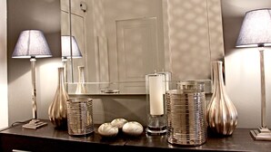 Zona de tocador bien iluminada con espejo, dos lámparas y varios objetos decorativos como jarrones y candelabros.