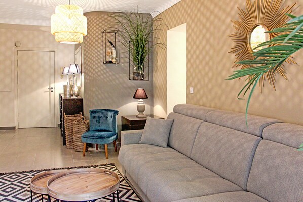 A living room with a grey sofa, wicker furniture, a blue chair, and a patterned rug.