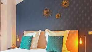 Una cama bien hecha con ropa de cama blanca y verde azulado, dos lámparas de noche y decoración en la pared.