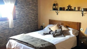 Ein ordentlich gemachtes Bett mit Kissen und Decke, ein hölzernes Kopfteil, ein Nachttisch mit Lampe, ein an der Wand befestigtes Regal mit Dekoration und ein Fenster mit Vorhängen.
