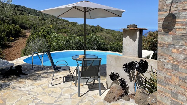 Ein Poolbereich mit Tisch, Stühlen, einem großen Sonnenschirm und einer Steinmauer.