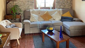Ein Wohnzimmer mit Steinwand, Holzboden, einer Chandelüstere, einer Sofagarnitur, einem Couchtisch und einer Pflanze.