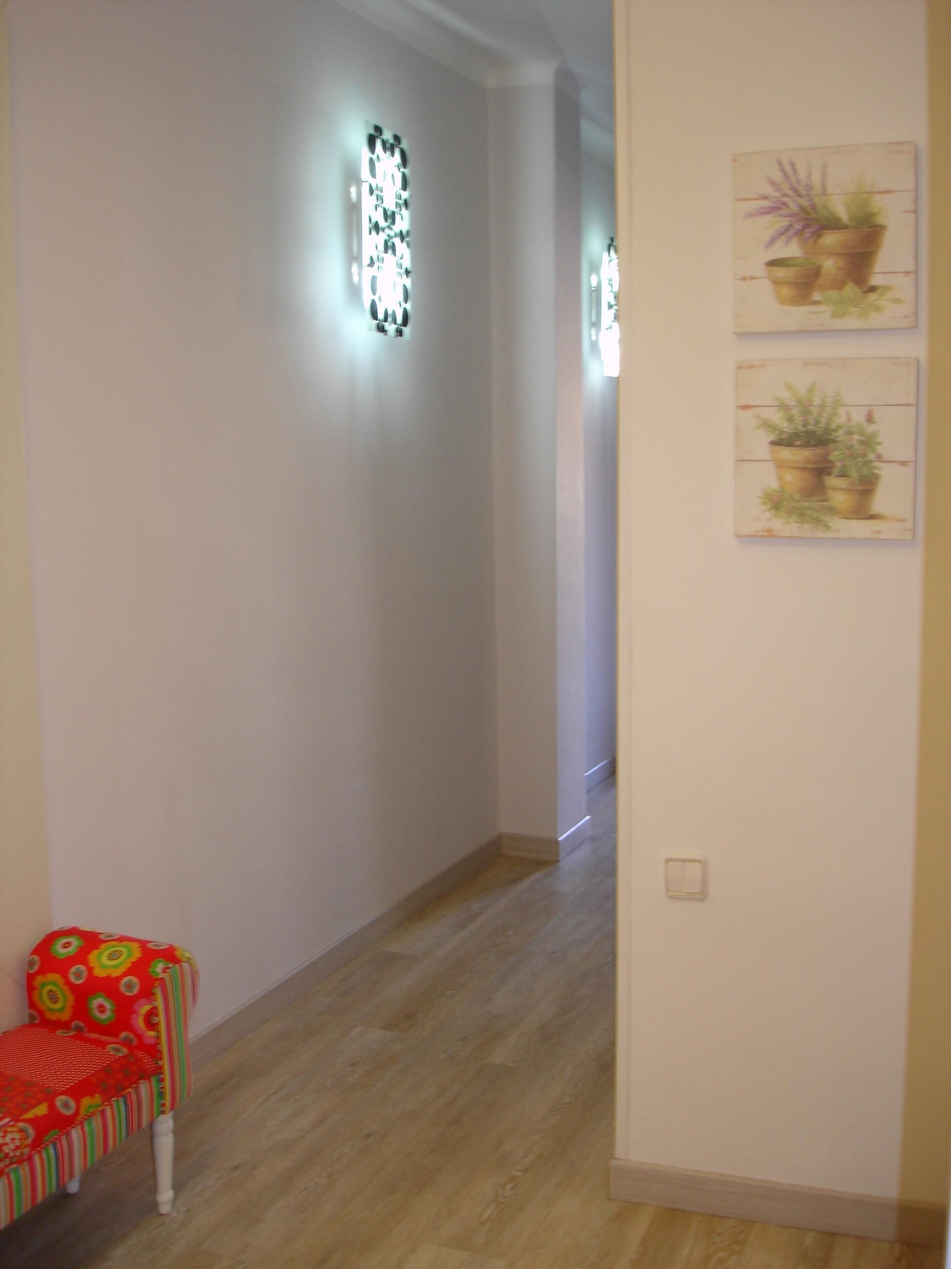 Ein schmaler Korridor mit Holzboden, einem roten Sessel mit Blumenmuster und zwei Wandleuchten.