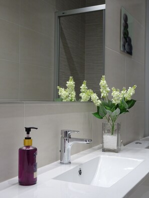 Un baño con un lavabo blanco, un espejo y un jarrón con flores blancas.