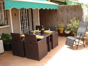 Un patio al aire libre con mobiliario de mimbre, una mesa dispuesta para comer y plantas en macetas.