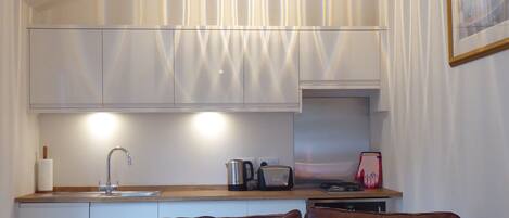 A modern kitchen with white cabinetry and a pendant light, a brown leather sofa, and a framed picture on the wall.
