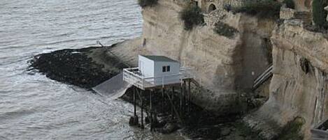 Eine Küstenklippe mit einem kleinen, weißen Gebäude auf Stelzen in der Nähe des Wassers.