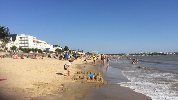 Ein Strand mit Menschen, Sandburgen und Gebäuden im Hintergrund.