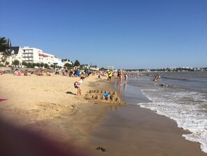 A beach with people, sandcastles, and buildings in the background.