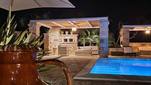 A stone patio with a pool, outdoor furniture, and a barbecue area at night. - Elegant villa with swimming pool in Salento  (Zona Centonze-Velodromo)
