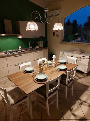 A dining area with a wooden table set for four, surrounded by white chairs. - Elegant villa with swimming pool in Salento  (Zona Centonze-Velodromo)