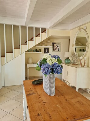 Une table à manger en bois ornée d’un vase de fleurs, un buffet blanc avec un miroir, et un escalier avec des rampes blanches.