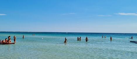 Una playa con agua turquesa cristalina, una orilla arenosa y gente nadando y relajándose.