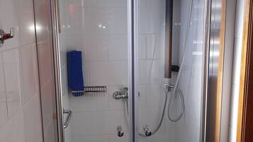 Un box de ducha con paredes de vidrio, suelo a cuadros, un cabezal de ducha de mano y un perchero para toallas.