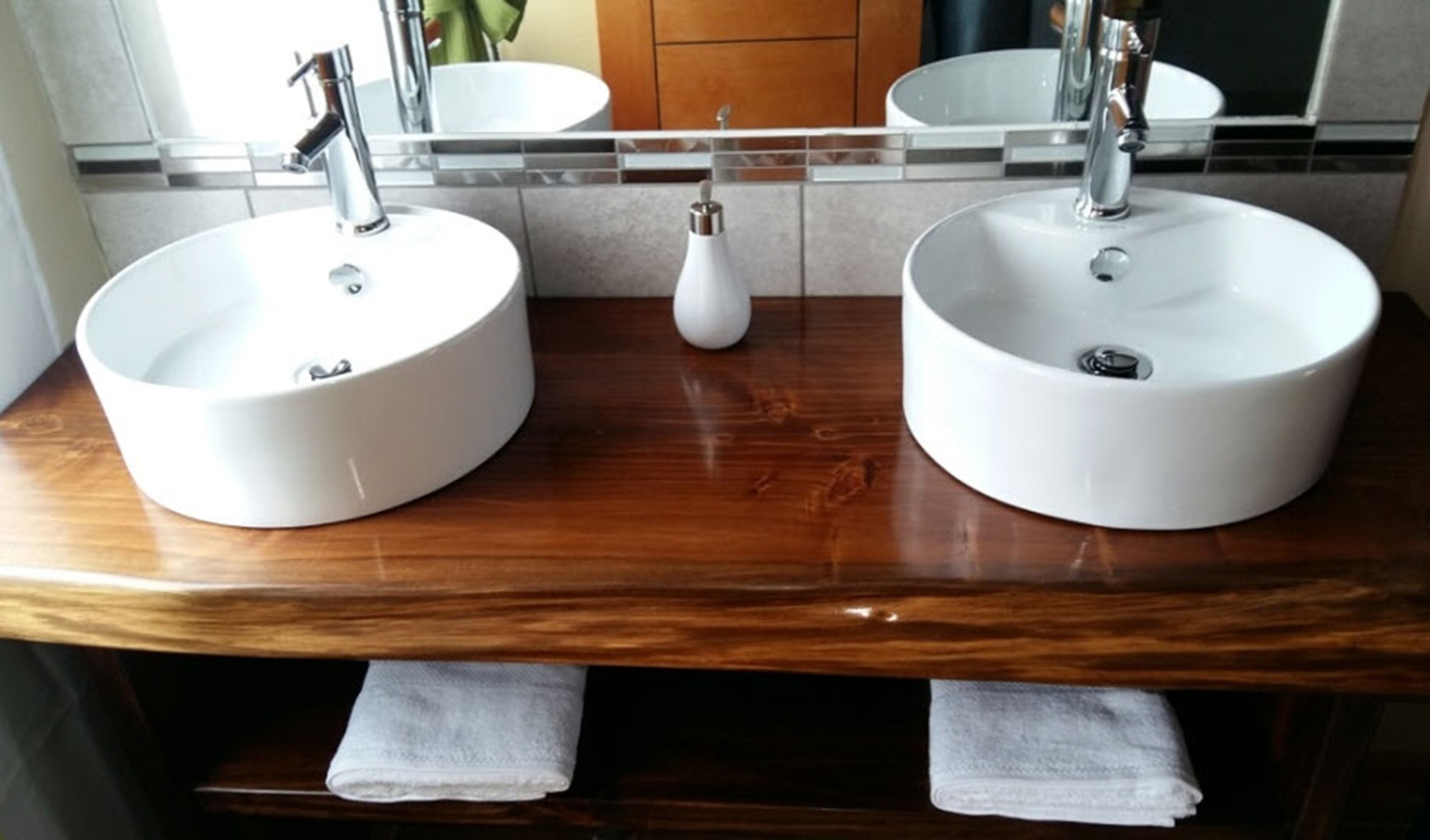 A bathroom with two round white sinks, a wooden vanity, and a mirror above the sinks.