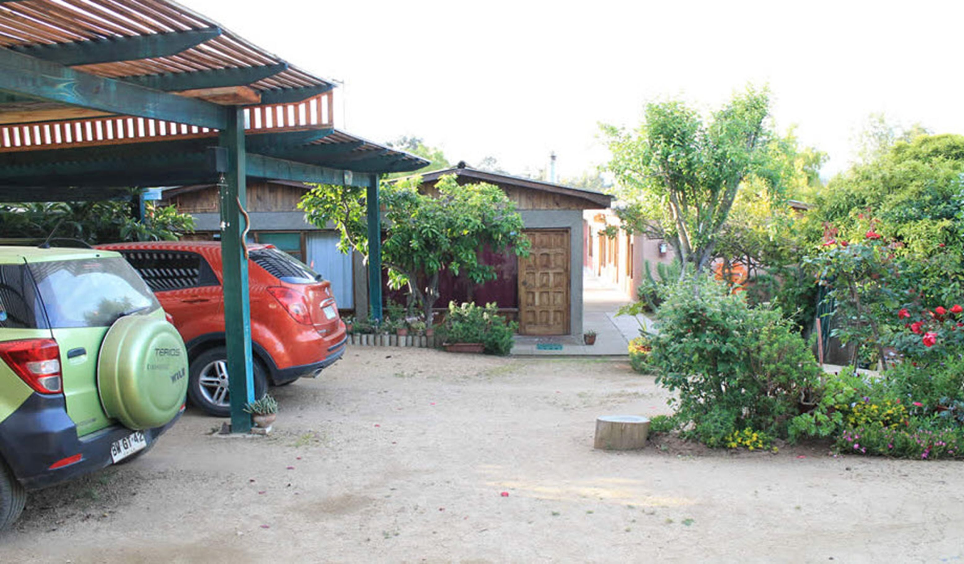 A parking area with two cars, a covered structure, and a garden with various plants and flowers.