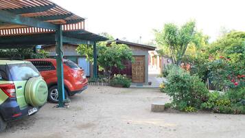 A parking area with two cars, a covered structure, and a garden with various plants and flowers.