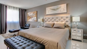 A modern bedroom with a large bed, a tufted headboard, two bedside tables with lamps, a bench, and a large abstract painting on the wall. - Casa Stefania - Marbellamar (Marbella)