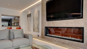 A modern living room with a sofa, a glass coffee table, a fireplace, and a large flat-screen TV mounted on the wall. - Casa Stefania - Marbellamar (Marbella)