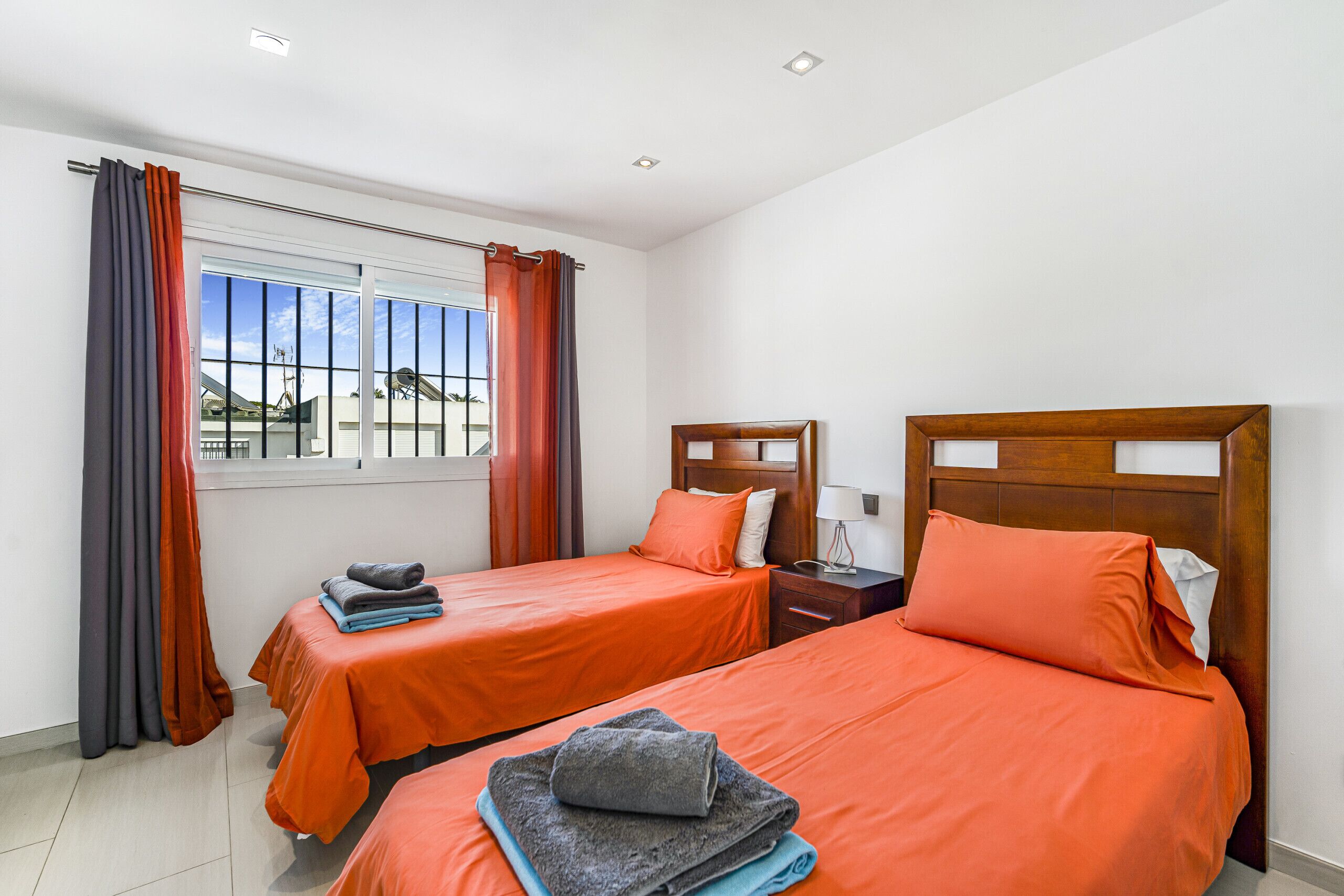 A hotel room with two beds, a window with curtains, a nightstand, and a view of buildings outside.