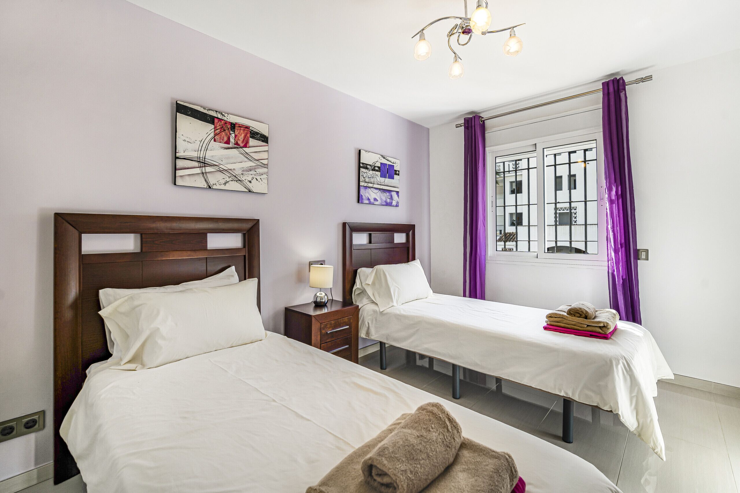 Een hotelkamer met twee bedden, een nachtkastje met een lamp, en kunstwerken aan de wanden.