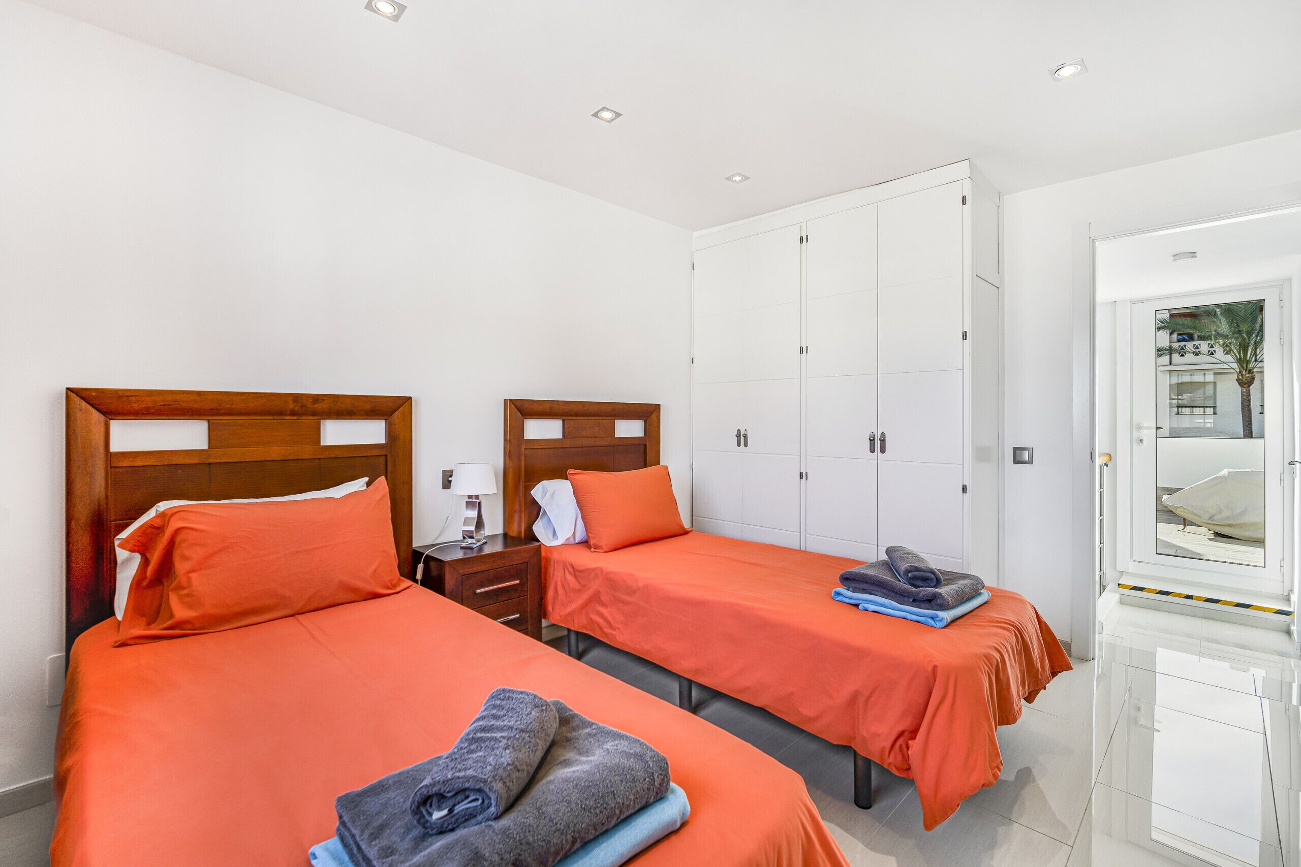 Une chambre d’hôtel avec deux lits, chacun agrémenté d’une literie orange, une table de chevet avec une lampe et une armoire à plusieurs portes.