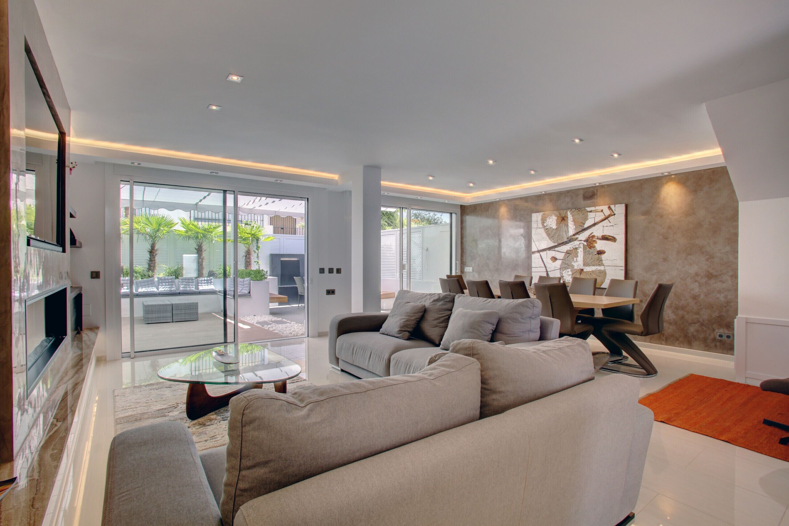 A modern living room with a large sofa, glass coffee table, and a dining area with chairs and a table.
