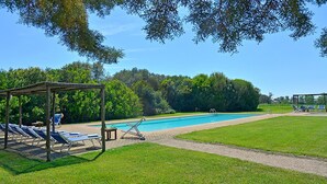 Una piscina con sillones de descanso y una zona de estar cubierta.